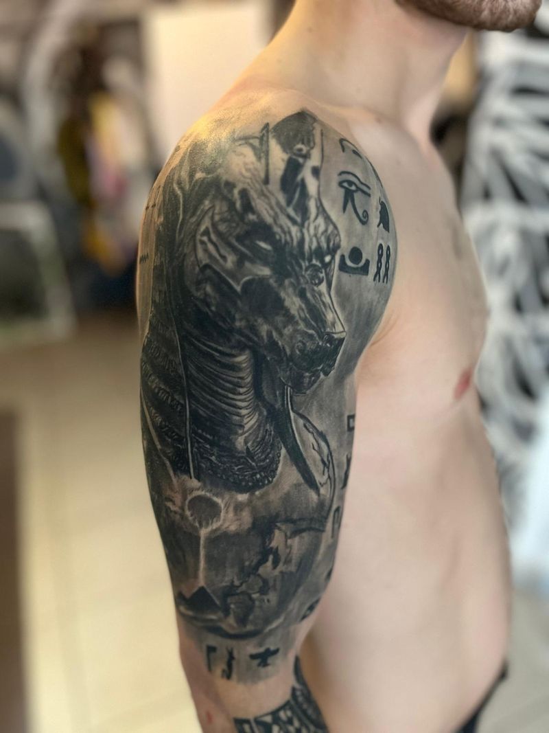 Black and grey realism half sleeve of Anubis with hieroglyphs, wrapping the shoulder