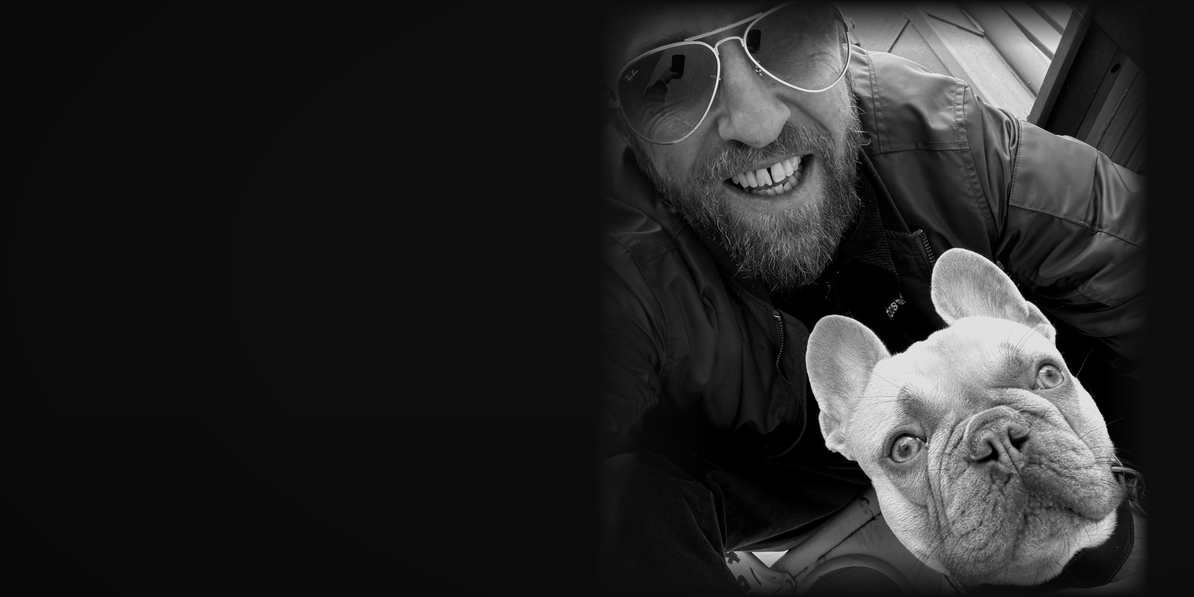 Stoyan smiling into the camera with Cox, the studio's French bulldog, looking up at him